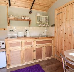 A small kitchen with wooden cabinets microwave toaster kettle and a dining table at Railway Carriage in Govilon