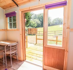 A small table with two chairs in a wooden room with an open door to a deck and grassy area at Railway Carriage in Govilon