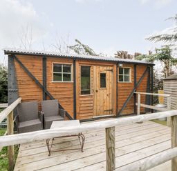 A wooden cabin with two wicker chairs and a table on a wooden deck at Railway Carriage in Govilon