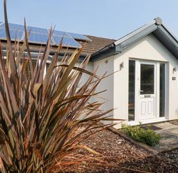 Exterior front view of a white house with solar panels on the roof and a tall plant in the foreground at Trenant View in Wadebridge