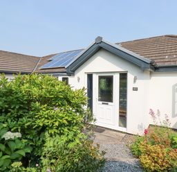 The front entrance of a single-story house with bushes and plants in front and solar panels on the roof at Trenant View in Wadebridge