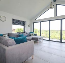 A living room with a large gray sectional sofa and glass sliding doors overlooking greenery at Trenant View in Wadebridge
