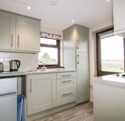 A kitchen with gray cabinets a small fridge a toaster kettle sink and stove with two windows and a door at Little May in Newquay