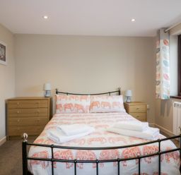 A bedroom with a double bed with orange patterned bedding two bedside tables with lamps a chest of drawers and a window with patterned curtains at Little May in Newquay