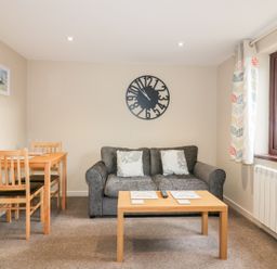 A living room with a grey sofa wooden coffee table dining table with chairs and a window at Little May in Newquay