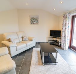 A living room with cream sofas a black glass coffee table a TV on stand and a glass door with floral curtains at Bothi in Llanuwchllyn