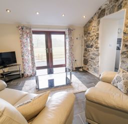 A living room with leather sofas glass coffee table and television near stone wall at Bothi in Llanuwchllyn