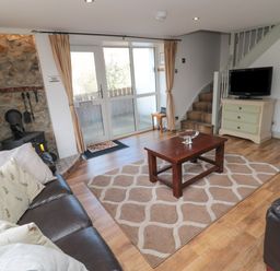 A living room with brown leather sofas a wooden coffee table a rug a wall-mounted stove a television on a dresser and stairs at Chillingham Cottage in Belford