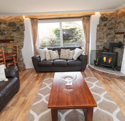 A living room with leather sofas a wooden coffee table stone walls and a wood burning stove at Chillingham Cottage in Belford
