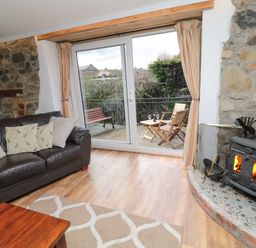 A living room with a leather sofa and wood burning stove next to patio doors opening to outdoor seating at Chillingham Cottage in Belford