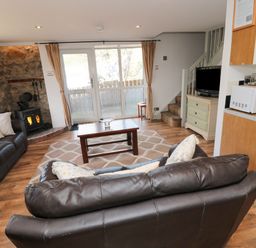 A living room with leather sofas a wooden coffee table a wood stove and a TV next to stairs at Chillingham Cottage in Belford