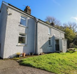 An exterior view of a white two-story house with multiple windows and a lawn with a picnic table near Pengraig near Tregaron