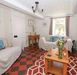 A living room with two sofas with cushions a wooden coffee table with flowers and a bottle a small wooden side table and a television near a window at Pengraig near Tregaron