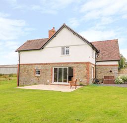 A stone and white two-story house with a tiled roof and a patio with a chair at The Old Farmhouse Upper Pitts in Knighton