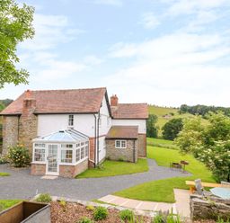 A house with a glass conservatory and garden furniture on a lawn with hills in the background at The Old Farmhouse Upper Pitts in Knighton