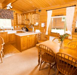A kitchen and dining area with wooden cabinets a table with chairs and curtains at Lodge 8 in Louth