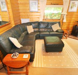 A living room with a dark green leather sectional sofa and ottoman with light cushions and wooden side tables at Lodge 8 in Louth