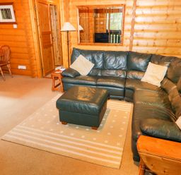 A living room with a green leather corner sofa and ottoman with a wooden dining table and chairs in Lodge 8 in Louth