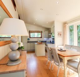 A dining area with a wooden table and wicker chairs next to glass doors with a kitchen in the background at Brooke in Exton Rutland
