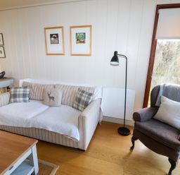 A living room with a striped sofa and patterned pillows next to an armchair with a cushion and throw blanket at Burley in Exton Rutland