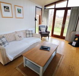 A living room with a sofa, armchair, wooden coffee table, wood stove, and glass doors leading outside at Burley in Exton Rutland