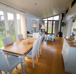 A dining area with six chairs and a wooden table next to glass doors and a living area with sofa armchair coffee table and fireplace at Burley in Exton Rutland