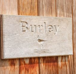 A wooden sign with the word Burley and a bird above water lines mounted on wooden planks at Burley in Exton Rutland
