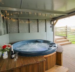 An outdoor covered patio with a hot tub flowers champagne and glasses on a wooden deck at Shepherds Cabin at Titterstone in Clee Hill