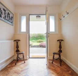 An entryway with two wooden chairs a radiator a painting of cows and an open door at Bower View in Madley