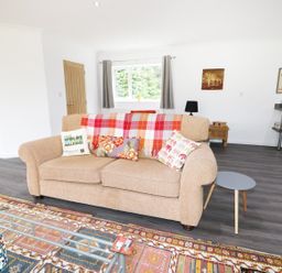 A living room with a beige sofa with cushions and a plaid throw a small round side table a patterned rug and a glass coffee table at Heron Lodge in Mavis Enderby near Spilsby