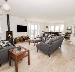 A living room with two gray sofas a glass side table a wood burning stove and a dining table at Manor House in Warkworth