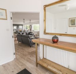 A hallway with a wooden console table and large mirror looking into a living room with gray sofas at Manor House in Warkworth