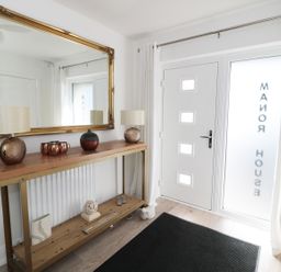 An entryway with a wooden console table holding lamps and decorative items a large mirror and a white door with frosted glass at Manor House in Warkworth