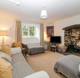 A living room with a sofa armchair ottoman television and a fireplace at Crannacombe Farmhouse in Loddiswell