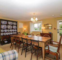 A dining room with a wooden table and mixed chairs including armchairs a cabinet with blue and white plates a sideboard with a mirror and lamps at Crannacombe Farmhouse Loddiswell