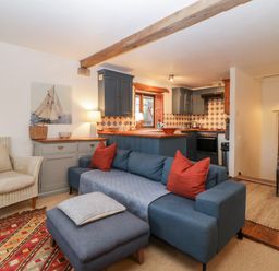 A living room with a blue sofa and red pillows next to a kitchen with blue cabinets and tiled backsplash at The Cider Barn in Loddiswell