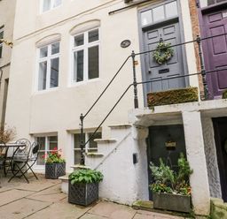 An outdoor patio with a metal table and chairs and several potted plants in front of a building with multiple doors in Robins Nest Whitby