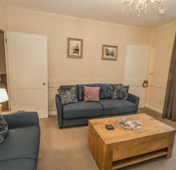 A living room with blue sofas a wooden coffee table a lamp and pictures on the wall at Robins Nest in Whitby