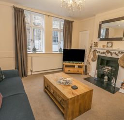 A living room with a sofa cushions and coffee table a television on a stand and a fireplace with stockings and a mirror at Robins Nest Whitby