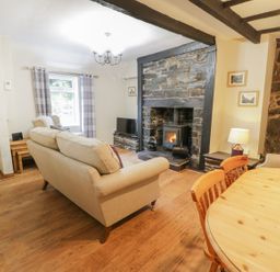 A living room with beige sofas a wood burning stove stone fireplace wooden dining table and chairs at Ty Coed in Llanberis