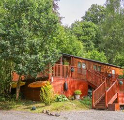A wooden cabin with stairs and railing surrounded by trees at Willow Lodge in Troutbeck Bridge