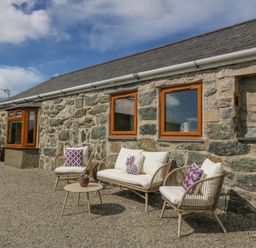 An outdoor seating area with chairs and a table against a stone wall at Beudy in Chwilog