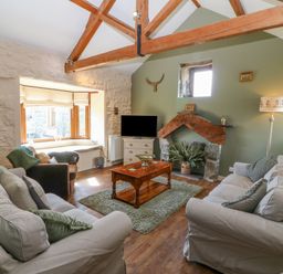 A living room with two sofas a wooden coffee table a fireplace and exposed wooden ceiling beams at Beudy in Chwilog