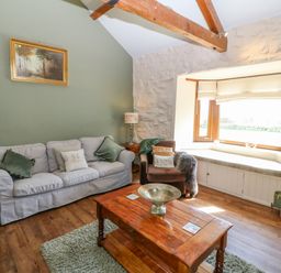 A living room with a sofa, armchair, wooden coffee table, window seat, and a framed picture on a green wall at Beudy in Chwilog