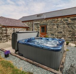 An outdoor hot tub with water jets in front of a stone building with a wooden door at Sgubor in Chwilog