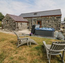 A stone house with a garden featuring two wooden chairs a hot tub and a picnic table at Sgubor in Chwilog