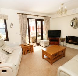 A living room with beige sofas a wooden coffee table a television and a wall-mounted fireplace at 5 Chandlers Yard in Burry Port