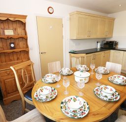 A kitchen with wooden cabinets a wooden dining table set with plates bowls and glasses at 5 Chandlers Yard in Burry Port