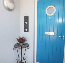 A blue front door with a round window and number 5 next to a metal table with a plant and a welcome sign at 5 Chandlers Yard in Burry Port