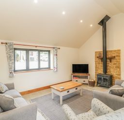 A living room with grey sofas a wooden coffee table a television and a wood stove with stone backdrop at The Milking Barn in Yeovil Somerset